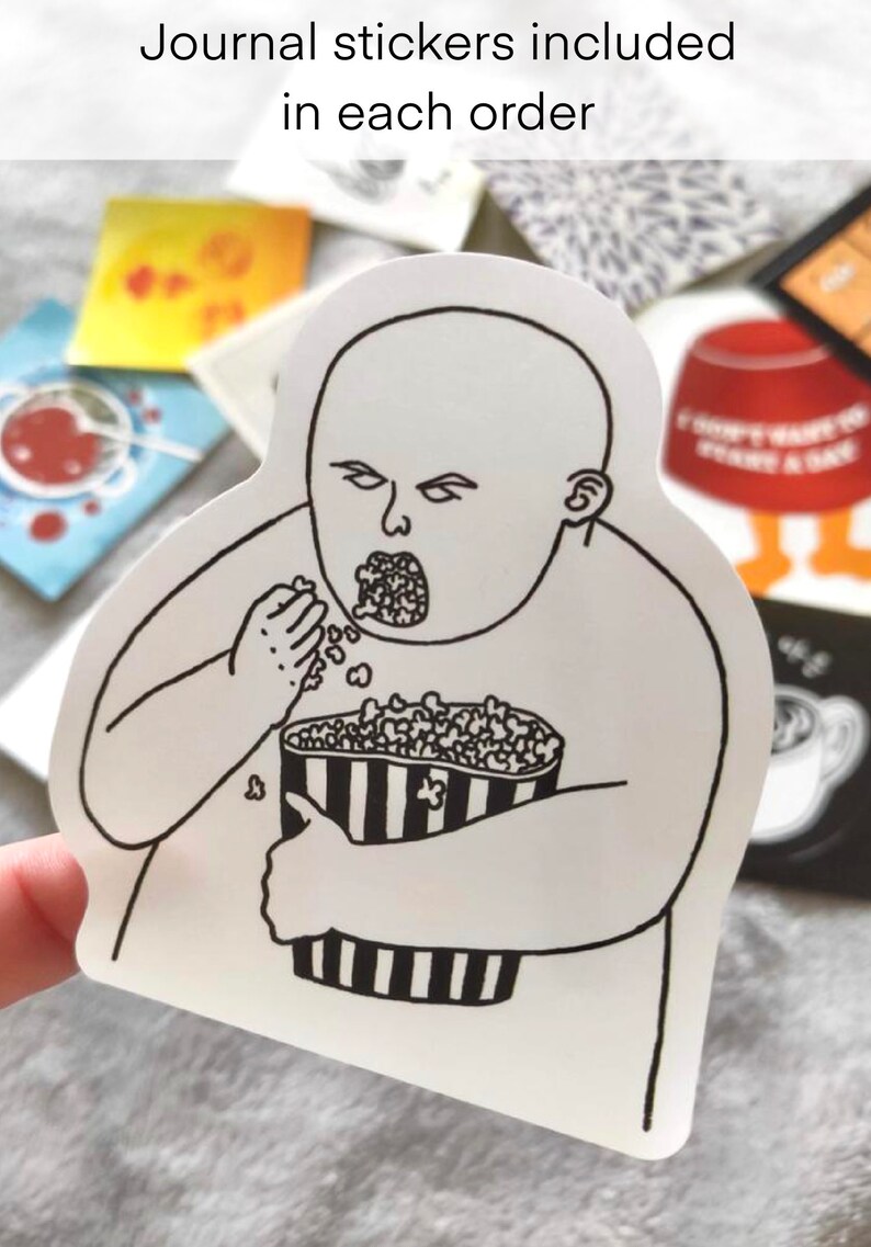 May include: A white sticker featuring a black and white illustration of a person eating popcorn from a striped container. The sticker has the text "Journal stickers included in each order" at the top.