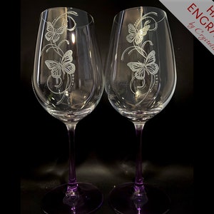 Op de afbeelding: Twee wijnglazen met paarse stelen en een handgegraveerd vlinderontwerp. De glazen zijn handgegraveerd met de tekst "HAND ENGRAVED by Cryselle".