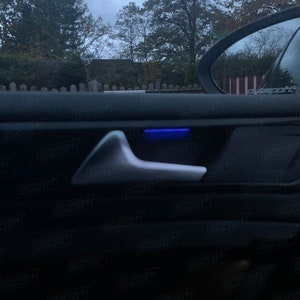 May include: A close-up of a car door handle with a blue light illuminating the handle. The handle is made of silver metal and is surrounded by black leather.