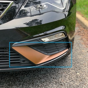 Peut inclure: Gros plan sur le pare-chocs avant d'une voiture noire avec un accent de couleur cuivre sur la calandre inférieure. L'accent est de forme triangulaire et s'étend du centre de la calandre jusqu'au bord du pare-chocs.