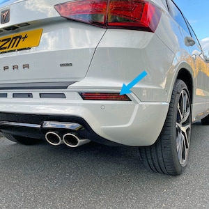 Könnte beinhalten: Heckansicht eines weißen SUV mit schwarzem Stoßfänger und zwei Auspuffrohren. Das Fahrzeug hat ein rotes Rückstrahlerlicht an der rechten Seite des Stoßfängers.