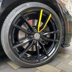 Könnte beinhalten: Ein schwarzer Autoreifen mit einem gelben Streifen an der Seite. Der Reifen ist mit "235/35 R 19 91Y" beschriftet und hat eine schwarze Felge mit einer silbernen Bremsscheibe. Der Reifen ist an einem schwarzen Auto montiert.