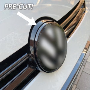 Puede incluir: Primer plano de la parrilla delantera de un coche con un emblema y molduras negras. El texto "PRE-CUT!" está encima del emblema, con una flecha blanca que apunta a la moldura negra. La carrocería del coche es blanca.