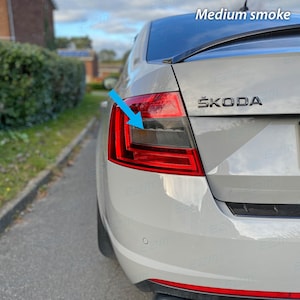 May include: A white Skoda car with a tinted rear light. The rear light is labelled "Medium smoke" and has a blue arrow pointing to it.
