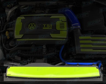 May include: A close-up of a car engine with a green and black engine cover. The cover has the Volkswagen logo and the word "TSI" on it. There is a blue hose running along the top of the engine.
