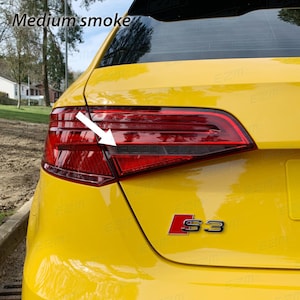 Könnte beinhalten: Ein gelber Audi S3 mit getönten Rückleuchten. Die Rückleuchten sind mittelstark getönt, wodurch sie dunkler erscheinen. Das Auto hat ein schwarzes S3-Emblem am Heck.