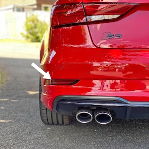 May include: A red Audi S3 with black trim and dual exhaust pipes. The car has a rear reflector light on the left side of the bumper.