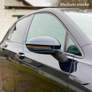 May include: A black car with a tinted side window and a black side mirror with a medium smoke tint. The mirror has a built-in turn signal.