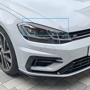 Könnte beinhalten: Ein weißes Auto mit schwarzer Frontstoßstange und schwarzen Scheinwerfern. Das Auto hat einen schwarzen Kühlergrill mit einem "R" Emblem.
