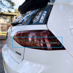 Puede incluir: Un coche blanco con luces traseras tintadas. Las luces traseras son de color rojo oscuro y tienen un borde negro alrededor de los bordes. El coche tiene una pegatina "MoreBHP" en la parte trasera.