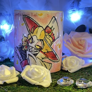 Może przedstawiać: Biały kubek ceramiczny z kreskówkową ilustracją postaci z czerwonymi włosami i żółtym kapeluszem. Postać ma na sobie czarny garnitur i szeroki uśmiech. Tekst "Paranoia" jest napisany na kubku kursywą.