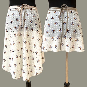 May include: A white wrap skirt with a floral print and a brown and blue colour scheme. The skirt has a tie at the waist and is made of a sheer fabric.