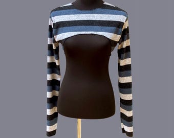 May include: A striped, long-sleeved bolero top in shades of blue, gray, and black. The top is displayed on a black mannequin. The sleeves are striped with horizontal bands of color. The bolero is a cropped style, exposing the midriff.