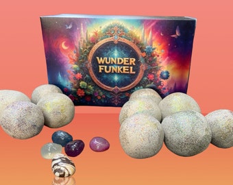 Op de afbeelding: Een display van glinsterende, bolvormige badbruisballen en kleurrijke edelstenen. De doos op de achtergrond bevat de tekst "Wunder Funkel" en de woorden "Entdeckt die Magie". De achtergrond is een verloop van roze en oranje.