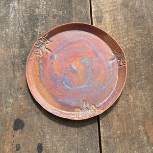 May include: A round, brown ceramic plate with a mottled glaze and a raised floral design around the edge.