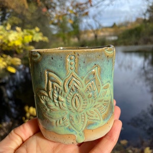 Peut inclure: Une tasse en céramique avec un glaçage vert et un motif de fleur de lotus en relief. La tasse a un glaçage brun moucheté sur le fond.