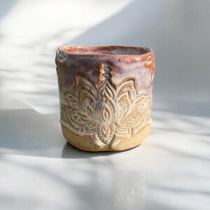 Może przedstawiać: Ręcznie wykonany ceramiczny kubek z kwiatowym wzorem. Kubek ma jasnobeżową podstawę, szczegółowy wytłoczony kwiat i gradient kolorów od jasnobeżowego do czerwonobrązowego na krawędzi. Widoczny jest tekst "Morgenträume".