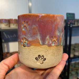 May include: A ceramic mug with a pink and white glaze. The mug has paw prints embossed on the bottom and sides.