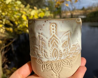 May include: A white ceramic mug with a brown glaze and a white floral design. The mug is speckled with brown flecks.