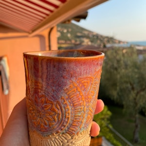 May include: A ceramic mug with a brown, orange and white patterned design. The mug is glazed with a speckled finish and has a rounded shape.