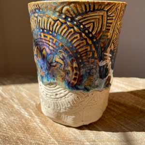 Könnte beinhalten: Eine Keramiktasse mit weißer Glasur und einem braunen und blauen Muster. Das Muster ist kompliziert und beinhaltet geometrische Formen und Linien.