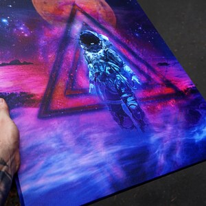 May include: A blue and purple space-themed painting with an astronaut floating in a triangle. The astronaut is wearing a white spacesuit and a helmet. The background is a nebula with a red planet.