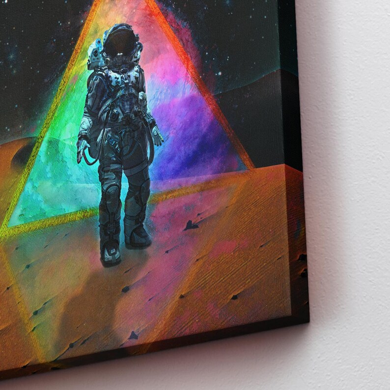 Op de afbeelding: Een astronaut in een zwart-wit ruimtepak staat op een rood, oranje en paars woestijnlandschap. Achter de astronaut bevindt zich een grote, kleurrijke driehoek met een donkerblauwe en paarse nevel erin.