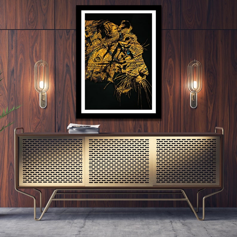 May include: A framed print of a gold and black animal head with a single blue eye. The animal is made up of dollar bills. The print is hanging on a dark wood wall above a gold metal cabinet.
