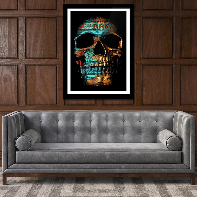 May include: A gold skull with a blue and red pattern, made from US dollar bills, on a black background. The skull is framed in a white frame and is hanging on a wood panel wall.
