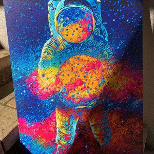 May include: A colorful abstract painting of an astronaut holding a large, round object in front of them. The astronaut is wearing a helmet and a spacesuit. The background is a dark blue with white stars.
