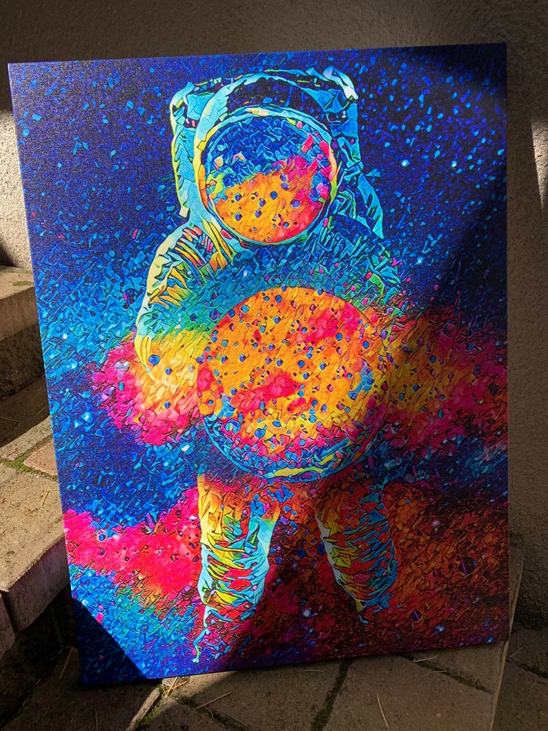 May include: A colorful abstract painting of an astronaut holding a large, round object in front of them. The astronaut is wearing a helmet and a spacesuit. The background is a dark blue with white stars.