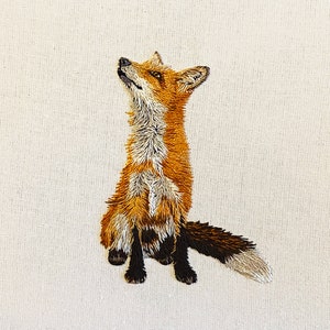 May include: A detailed embroidered fox with a white background. The fox is sitting up with its head tilted up and its tail curled behind it. The fox is brown, orange, and white.