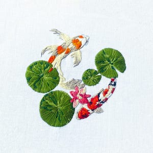 May include: Embroidered design of two koi fish swimming among green lily pads and a pink flower. The fish are white with orange and red markings.