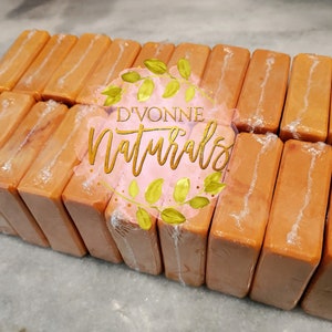 May include: A stack of orange-colored soap bars wrapped in clear plastic. The bars are arranged in rows and are labeled "D'VONNE Naturals".