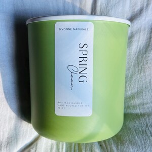 Op de afbeelding: Een lichtgroene sojawas kaars met een witte rand. Het etiket leest "Spring Clean" en "D'Vonne Naturals". De kaars is met de hand gegoten en is 369 gram.