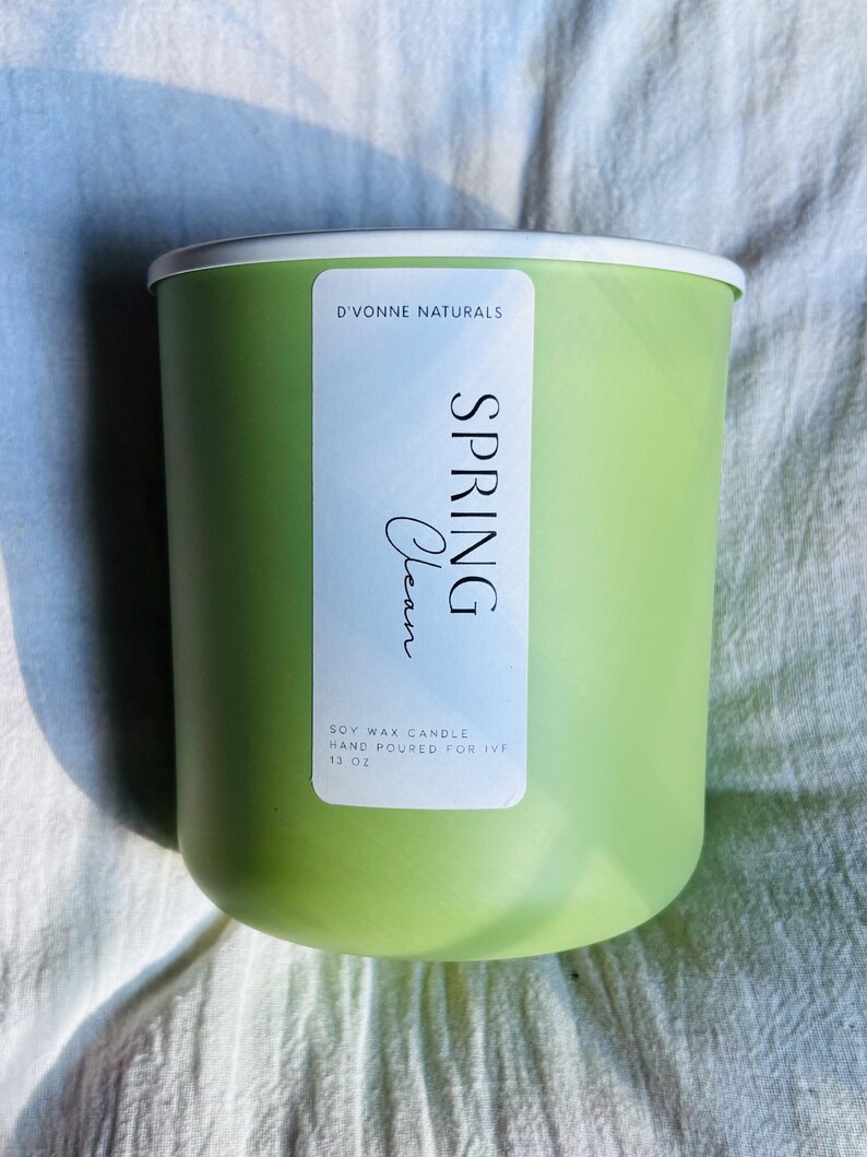 Op de afbeelding: Een lichtgroene sojawas kaars met een witte rand. Het etiket leest "Spring Clean" en "D'Vonne Naturals". De kaars is met de hand gegoten en is 369 gram.