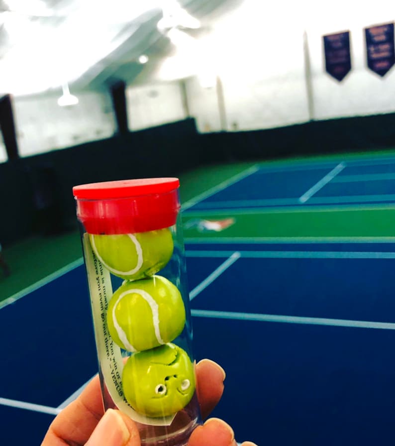 May include: A clear plastic tube with a red lid contains three miniature tennis balls. The tube has a white label with the text "This is literally your "You win" of VENUS W..."