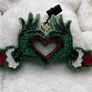 May include: Green glitter ornament shaped like two hands making a heart shape with a red glitter heart inside.