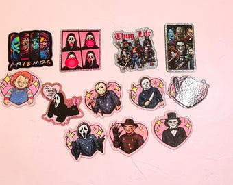 Puede incluir: Una colección de pegatinas con temática de películas de terror que presentan varios personajes icónicos. Los diseños incluyen una parodia de Friends, Ghostface, Chucky, Jason Voorhees, Freddy Krueger y Billy, con bordes en forma de corazón.