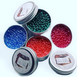 May include: Six small round metal tins with lids. Each tin contains a different colored gel bead air freshener. The lids have labels with the text "Lost Hidden Treasures" and the names of the scents: "Fruity Pebbles" and "Bikini Bottom".