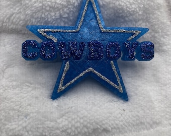 May include: A blue star with a silver outline and the word "COWBOYS" in blue glitter.