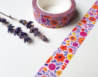 May include: A roll of pink washi tape with a floral pattern featuring orange, yellow, and pink flowers. The tape is on a white surface.
