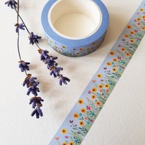 Könnte beinhalten: Eine Rolle blaues Washi-Tape mit einem Blumenmuster mit gelben, orangefarbenen und rosa Blüten auf grünem Hintergrund. Das Band ist abgewickelt und zeigt das Muster.