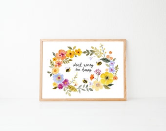 May include: Framed watercolour print with a floral wreath design. The wreath includes yellow, orange, and purple flowers, green leaves, and three bees. The text "don't worry bee happy" is in the centre of the wreath.