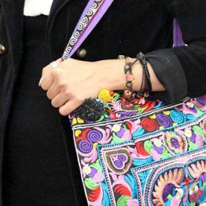 May include: A black shoulder bag with a purple strap and colourful embroidered floral design. The bag has a pom-pom detail.