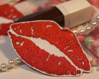 Puede incluir: Parche de labios bordados de color rojo con contorno blanco. El parche está hecho de tela y tiene una superficie texturizada.