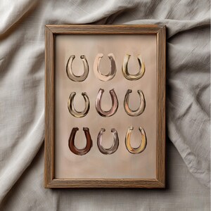 Puede incluir: Un marco de madera rectangular que contiene una impresi&oacute;n con nueve ilustraciones de herraduras dispuestas en una cuadr&iacute;cula de tres por tres. Cada herradura presenta un tono marr&oacute;n distinto, desde beige claro hasta chocolate, sobre un fondo beige.