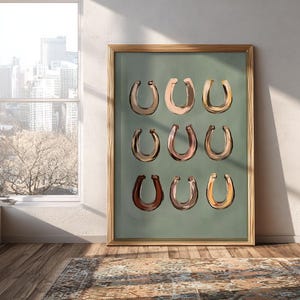 Puede incluir: Una l&aacute;mina de arte enmarcada que presenta una cuadr&iacute;cula de nueve ilustraciones de herraduras en varios tonos de marr&oacute;n, bronceado y oro met&aacute;lico, sobre un fondo verde salvia s&oacute;lido. El marco de madera tiene un acabado marr&oacute;n claro natural.