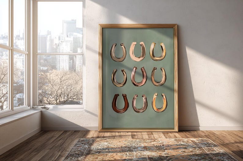 Puede incluir: Una l&aacute;mina de arte enmarcada que presenta una cuadr&iacute;cula de nueve ilustraciones de herraduras en varios tonos de marr&oacute;n, bronceado y oro met&aacute;lico, sobre un fondo verde salvia s&oacute;lido. El marco de madera tiene un acabado marr&oacute;n claro natural.