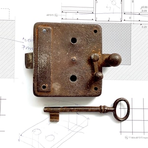 Peut inclure: Une serrure de porte en métal rouillé avec une clé. La serrure est de forme carrée avec un bouton rond sur le côté droit. La clé est en métal et a une tête ronde.